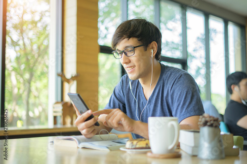 Young man texting message on smart phone while listening to music on earphones and enjoying free wireless internet connection at coffee shop