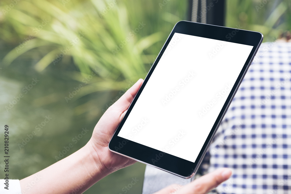 Mockup image of hands holding black tablet pc with white blank desktop screen with green nature background Mockup image of hands holding black tablet pc with white blank desktop screen with green nature background