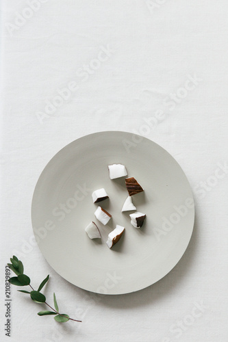 A collection of coconut bites on a neutral plate seen from above on a white surface.