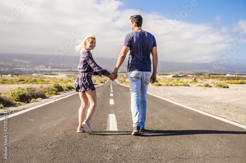 nice caucasian couple in relationship taking hands and walk together on a long way road straight to the future. life forever in coule and family in love concept. beautiful landscape and desert place