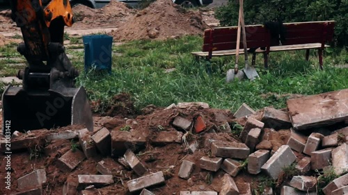 excavator bucket destroys the old road out of bricks.close-up photo