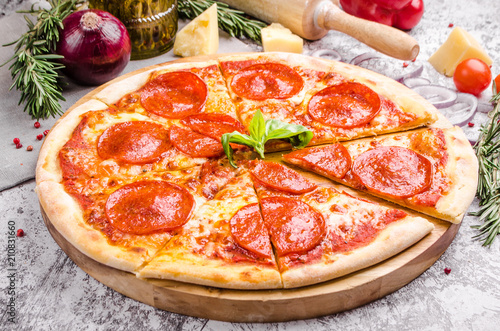 Homemade Meat Salami pizza with pepperoni sausage, bacon, onions, tomatoes, cheese on a wooden board over stone table background, restaurant menu concept. Italian food style, closeup.