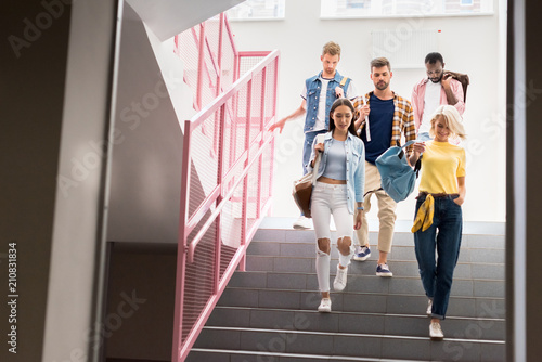 Stylish young students walking down on stairs of college corridor