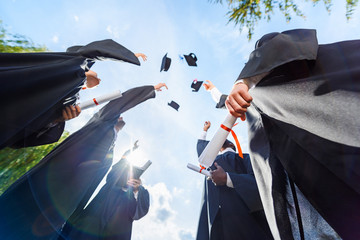 Bottom view of graduated students throwing up hats in front of blue sky