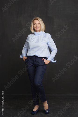 Full length portrait of attractive middle aged woman standing against dark background 