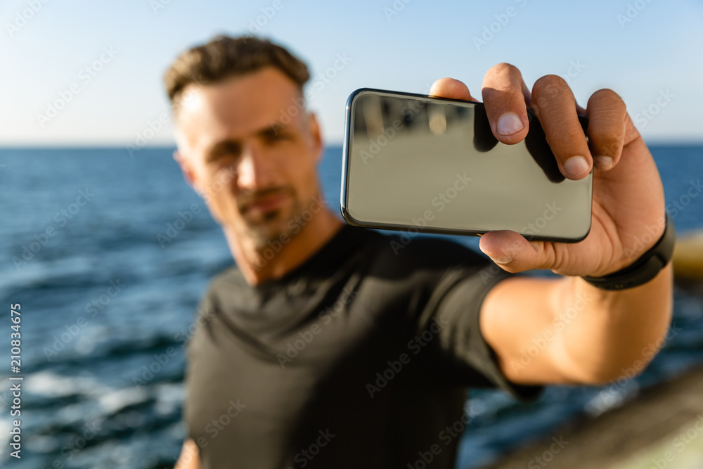close-up portrait of adult man taking selfie with smartphone on seashore