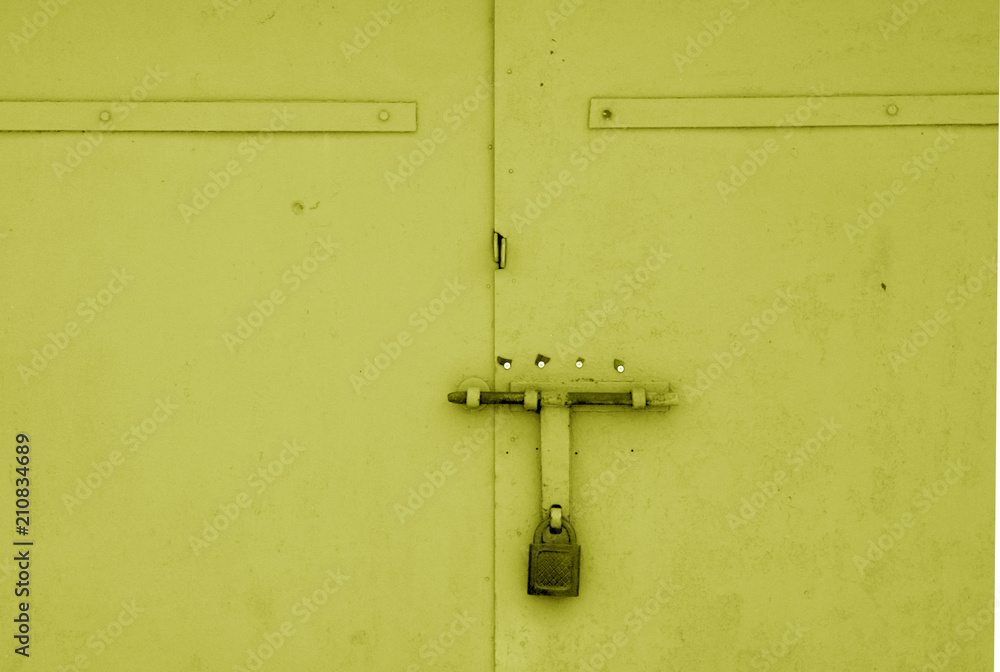 Old padlock on metal gate in yellow color.