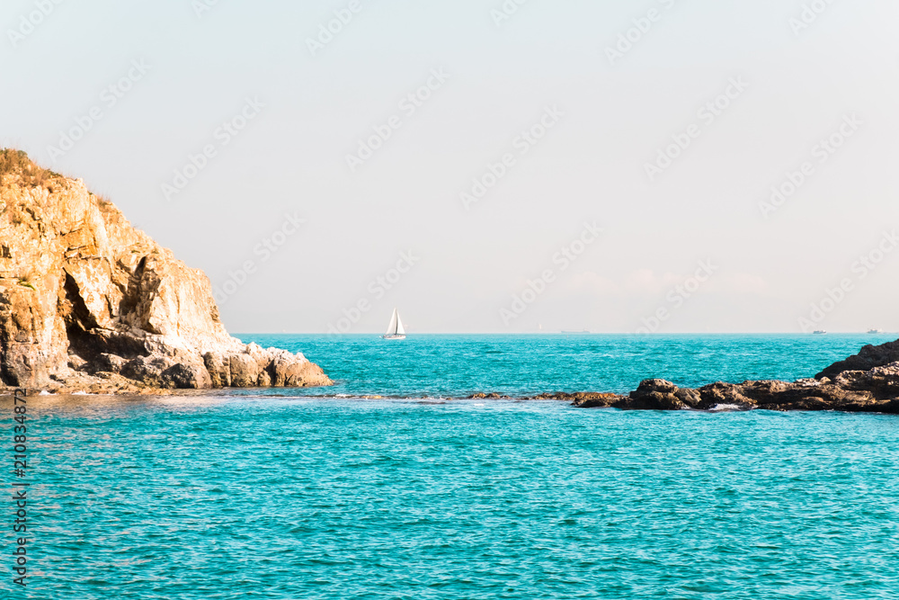 Fototapeta premium Two small rock islands in open sea connected with narrow isthmus. Lonely sailing boat with white sails . Beautiful romantic landscape, seascape. Natural background with copy space.