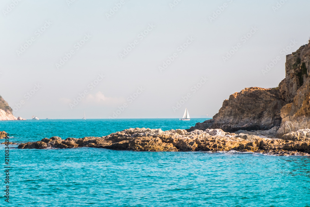 Two small rock islands in open sea connected with narrow isthmus. Lonely sailing boat with white sails . Beautiful romantic landscape, seascape. Natural background with copy space.