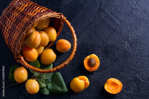 Tableau sur toile Delicious ripe apricots in a basket on black background, close-up, space for text