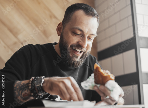 Young bearded man eating burger and smiling close up.