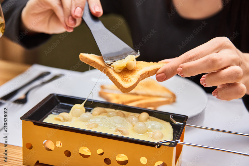 the girl tastes cheese raclette in a cafe. swiss food. cheese raclette with mushrooms on coupelles - special small skillet for a raclette