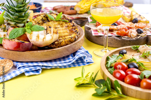 Different fruits and vegetables on grilled and shrimp. Yellow background. Summer dinner. Copy space.