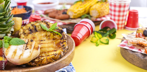 Different fruits and vegetables are cooked on the grill. Yellow background. Summer dinner. . Copy space.