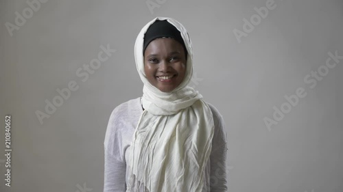 Young african muslim girl in hijab is standing and smiling, watching at camera, religioun concept, grey background photo