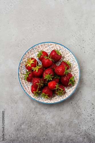 Fresh strawberries on light plate on gray old concrete background. Top view.