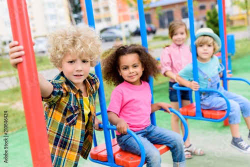 multicultural group of little children riding on swings at playground