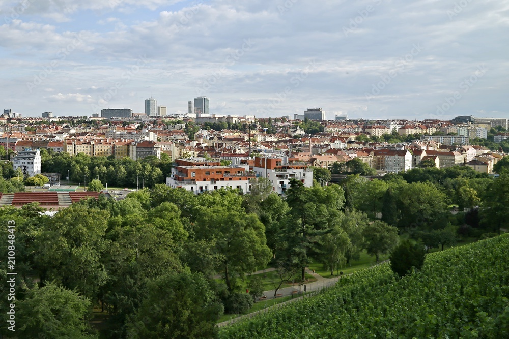 Panoramic view of Prague city from Grebovka park with old and modern buildings with red roofs, green trees, summer day with white clouds