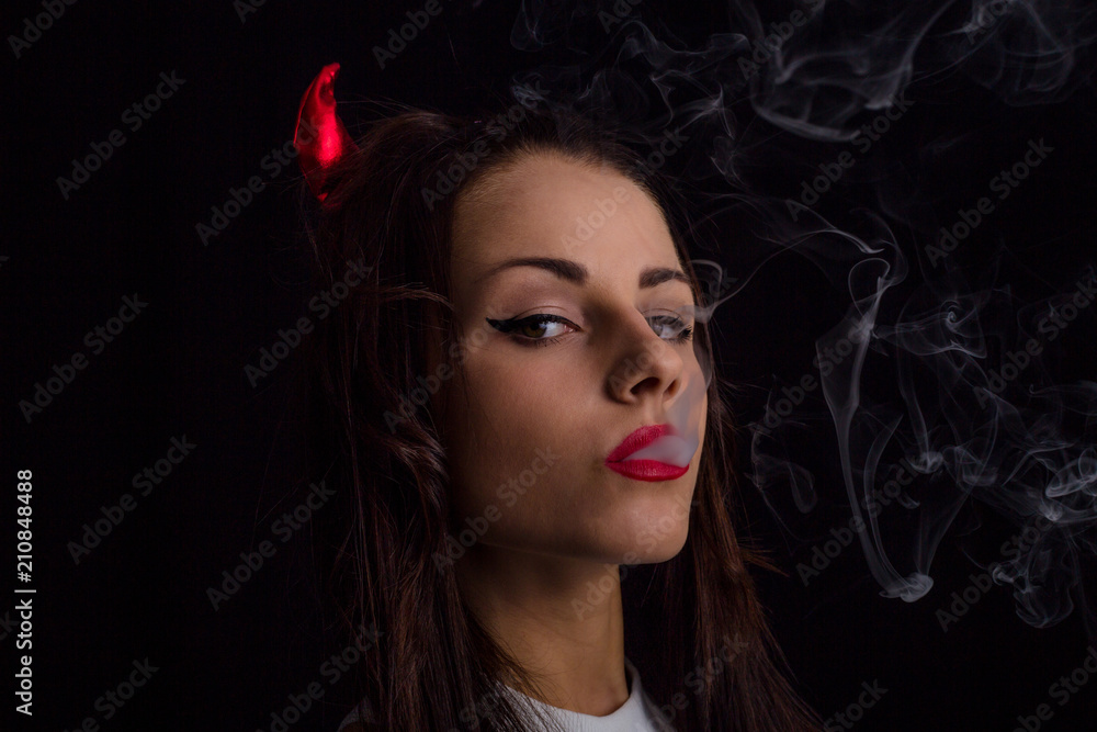 Portrait of young woman with red devil horns on head and cigarette smoke Portrait of young woman with red devil horns on head and cigarette smoke