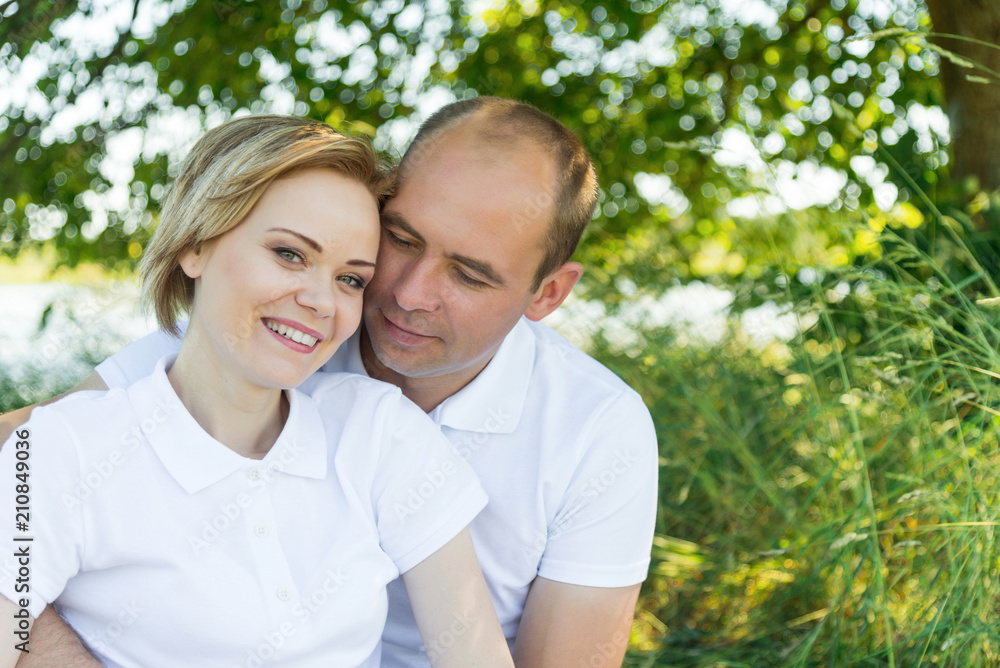 ouple in love. Man and woman in an embrace. A couple sitting in the grass in white T-shirts. ouple in love. Man and woman in an embrace. A couple sitting in the grass in white T-shirts.