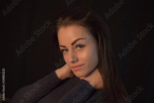 Beautiful young girl wearing sweater posing on black studio background touching her head with hand