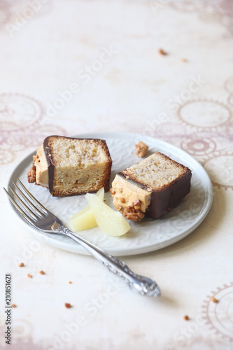 Two Pieces of Almond Pear Loaf Cake covered with Chocolate Glaze, topped with Caramel Cream Cheese Frosting and decorated with Spicy Crumble, on light beige background. 
