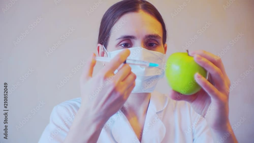 Portrait of a female doctor who makes an injection into ripe apple Portrait of a female doctor who makes an injection into ripe apple