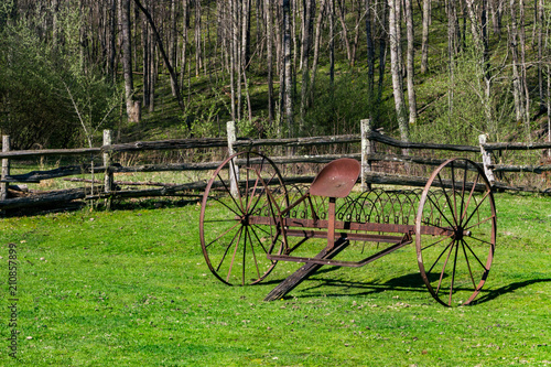 Antique farm equipment with big wheels on green grass in front of an old fence.