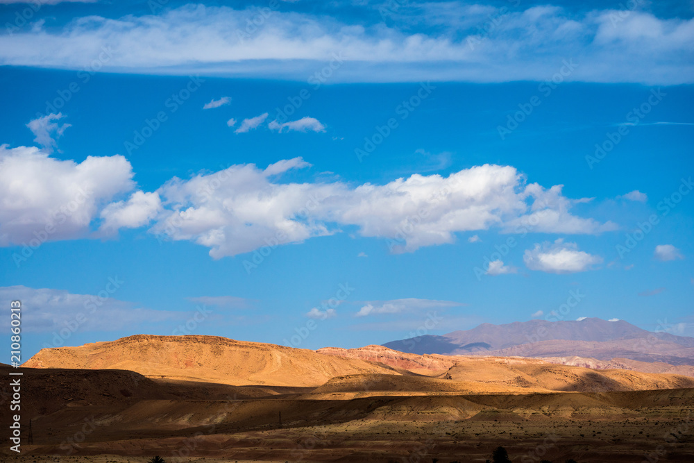 African landscape with sand dunes and Atlas mountain in Sahara desert with bright blue sky and clouds in Morocco
