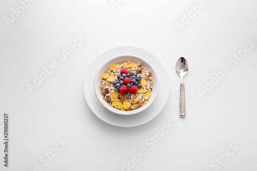 Muesli cereal breakfast with berry fruit in a white bowl with a spoon on the side viewed directly from above. Fresh rich in fiber granola dish viewed from above. Top view. Copy space © virtustudio