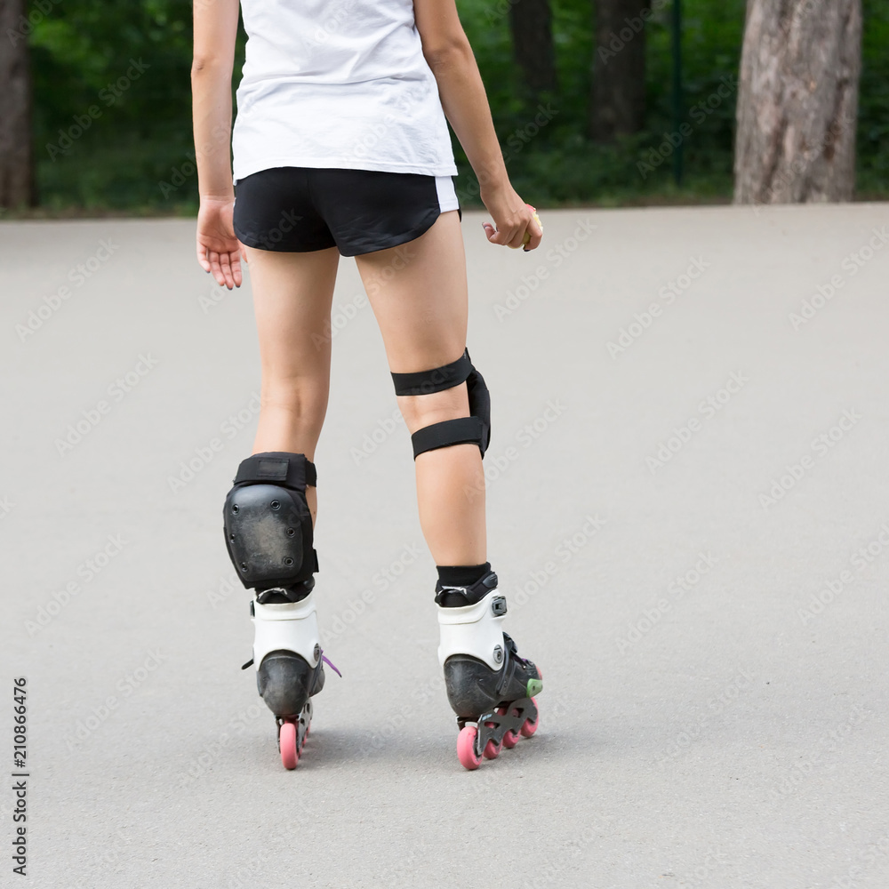Close up beautiful slim legs of young girl in short shorts wearing roller  skating in a sunny day in summer in the park. Knee protectors Stock Photo