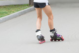 Close up beautiful slim legs of young girl in short shorts wearing roller skating in a sunny day in summer in the park