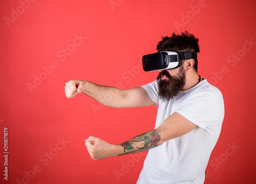 Man with beard in VR glasses driving car, red background. Virtual racing concept. Guy play racing game in VR. Hipster on aggressive face driving car on high speed in virtual reality