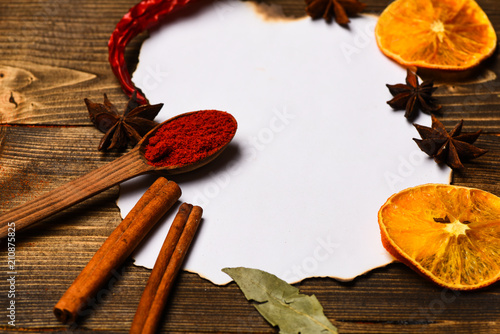Spices, kitchen herbs lay around white paper. Culinary recipe concept. Cinnamon, dried orange and pepper, star anise lay around blank paper for recipe, copy space. Piece of paper on wooden background