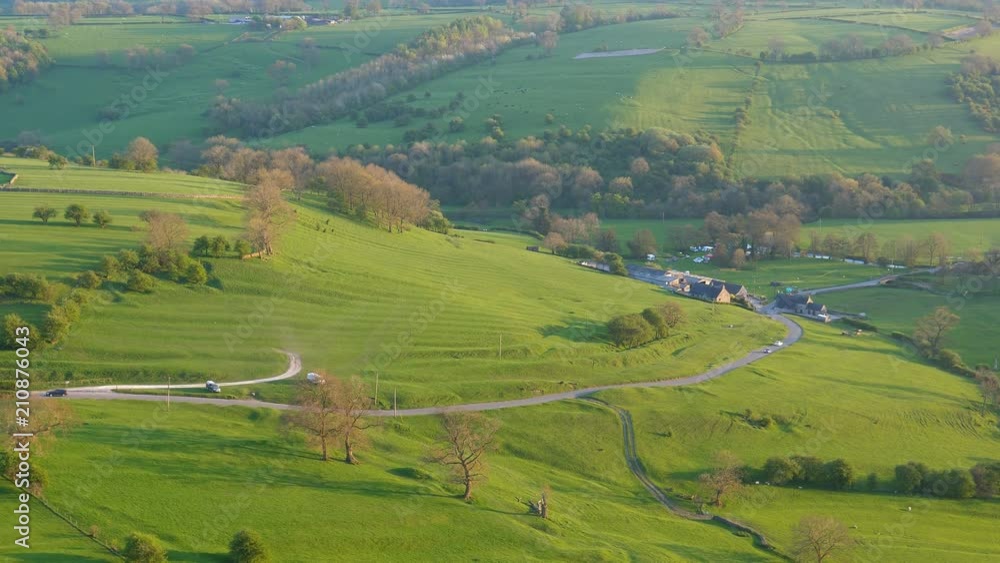 Magnificent Peak District National Park scenery from hilltop in the evening. Cars driving rural road, hills and Thorpe village in a valley lit by sun before sunset Magnificent Peak District National Park scenery from hilltop in the evening. Cars driving rural road, hills and Thorpe village in a valley lit by sun before sunset