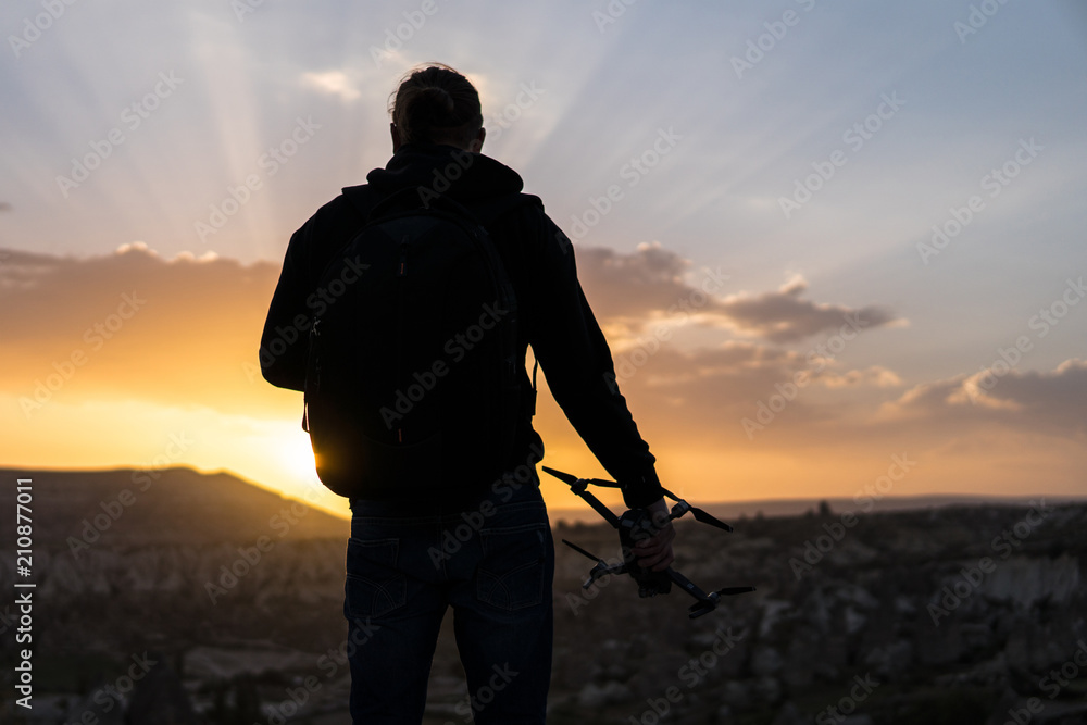 Back view of man standing against sunrise with drone in hand