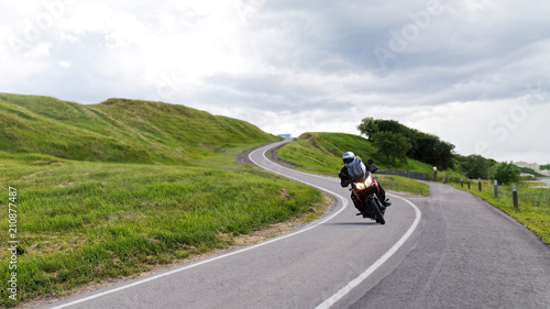 Alone motorcyclist rides along a narrow winding road among the green hills © mark_ka