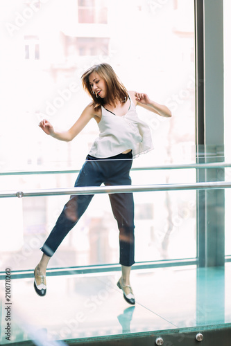 Smiling woman in stylish clothes jumping in shopping centre.Woman portrait indoors. Fashion lifestyle portrait of pretty woman.