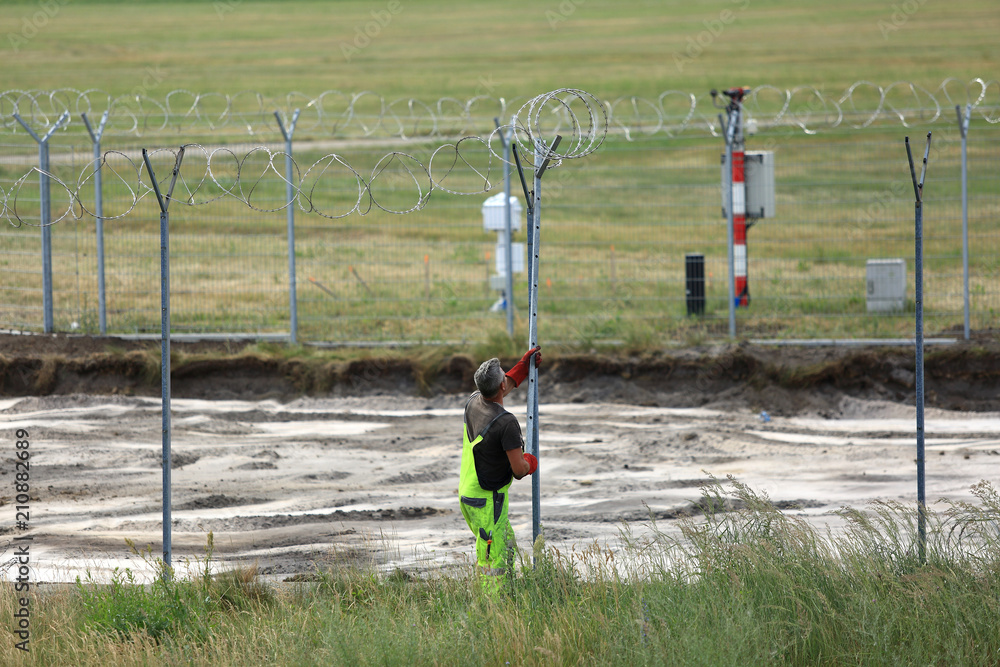 Budowa ogrodzenia, zakładanie drutu kolczastego wokół lotniska w Pyrzowicach. - obrazy, fototapety, plakaty 