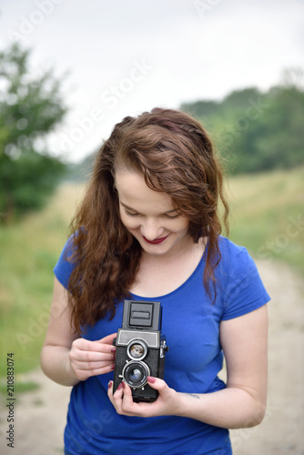 Beautiful young girl smiling while taking picture with vintage twin-lens reflex camera
