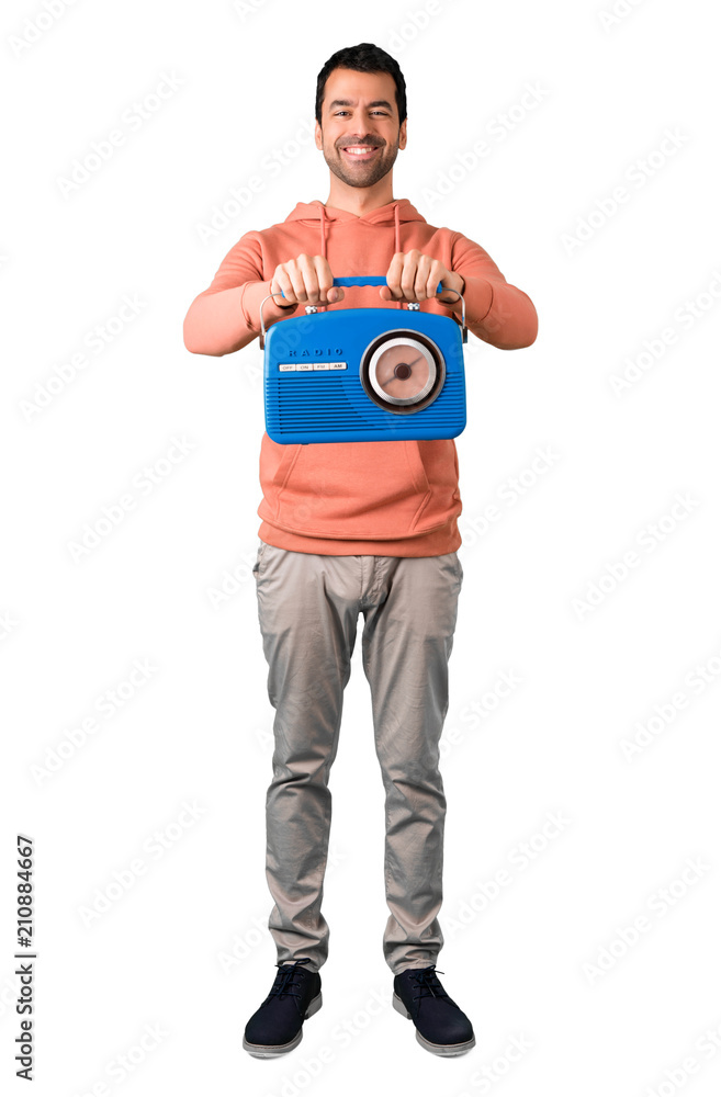 Full body of Man in a pink sweatshirt holding a blue vintage radio on isolated white background Full body of Man in a pink sweatshirt holding a blue vintage radio on isolated white background