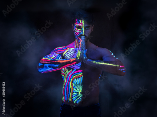 Foto Young man painted in fluorescent paint on face and muscular torso, in studio sho