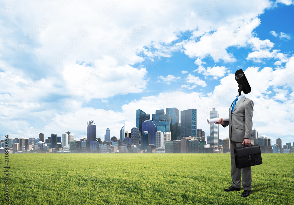 Camera headed man standing on green grass against modern cityscape Camera headed man standing on green grass against modern cityscape