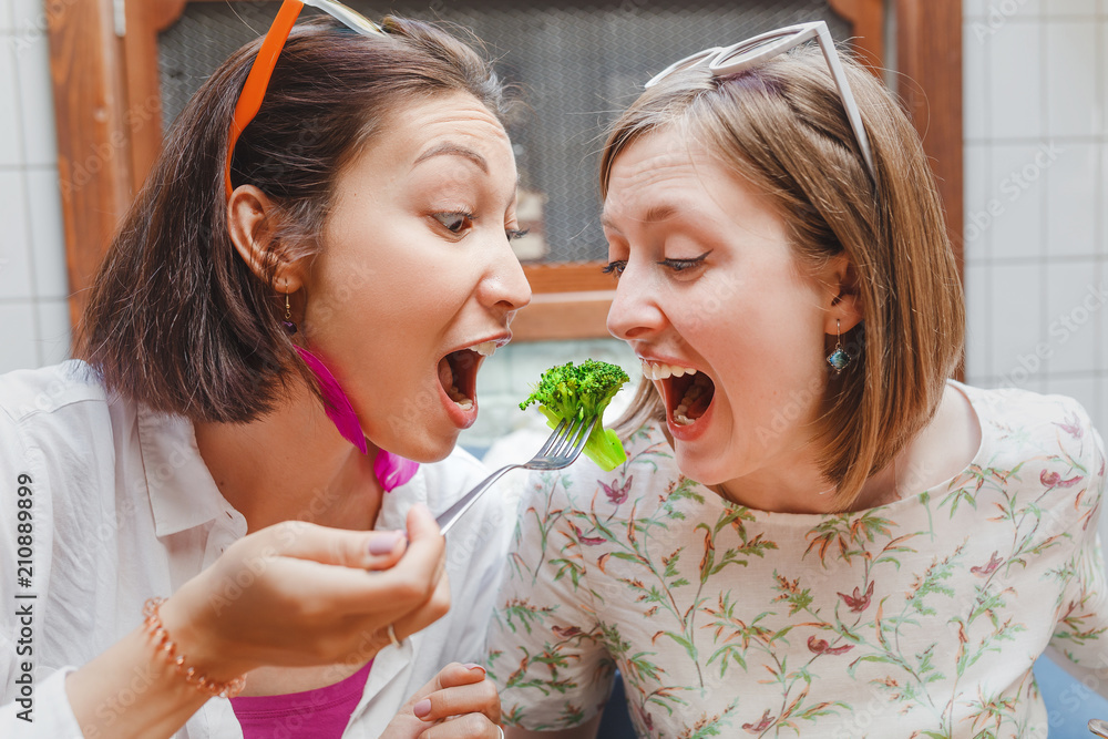portrait of two girls friends eating broccoli with one fork