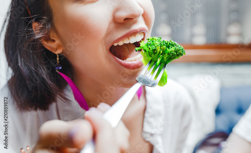Portrait of happy smiling young casual woman eating broccoli in restaurant