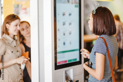 Obraz na plátně Group of people, friends ordering food at the touch screen self service terminal