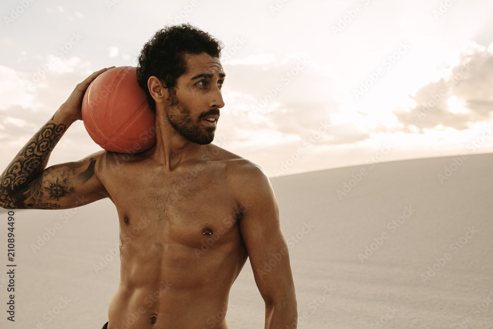 Muscular man with a exercise ball in desert Muscular man with a exercise ball in desert