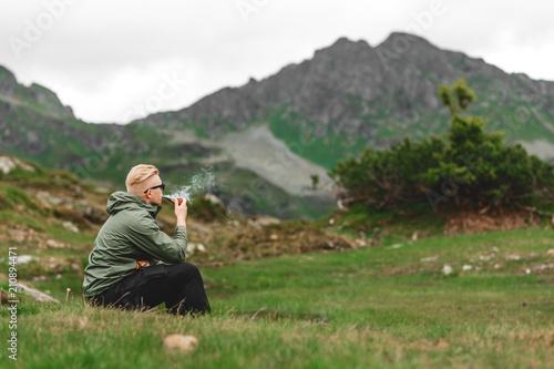 Mann wandert durch die Berge, sitzt und raucht Pfeife