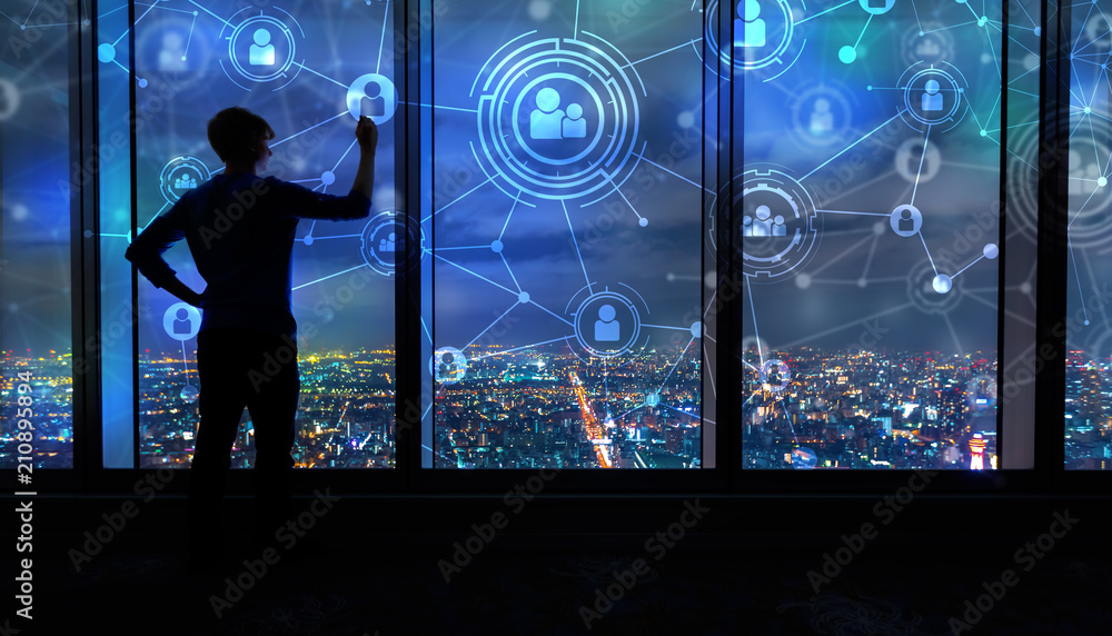 Social Connections with man writing on large windows high above a sprawling city at night Social Connections with man writing on large windows high above a sprawling city at night