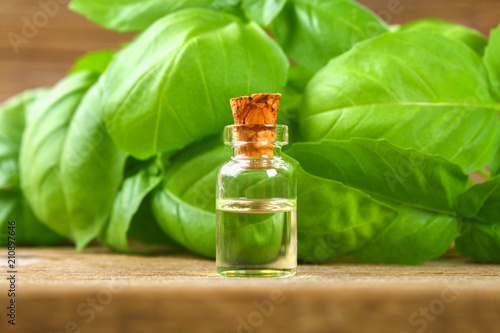 A bottle of basil essential oil with fresh basil leaves on a table.